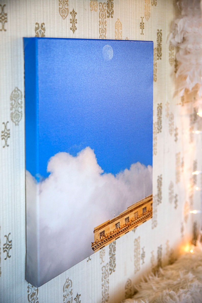 Pode incluir: Uma impress&atilde;o em tela de um edif&iacute;cio com um c&eacute;u azul e nuvens brancas. O edif&iacute;cio est&aacute; parcialmente obscurecido pelas nuvens.