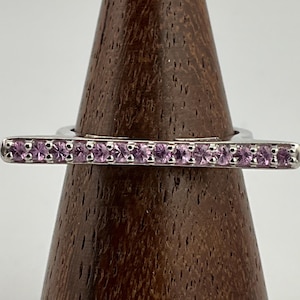 May include: A silver ring with a row of pink gemstones set in a straight band.