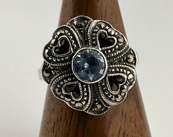 Puede incluir: Un anillo de plata con una piedra preciosa azul rodeada de un diseño floral con detalles de marcasita.