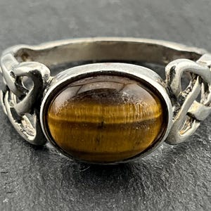 May include: A silver ring featuring a Celtic knot design and a brown tiger's eye gemstone.