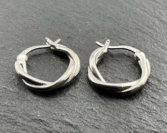 May include: A pair of silver-colored hoop earrings. Each earring features a twisted design, with the metal appearing to be smooth and reflective. The earrings are displayed on a dark, textured surface.