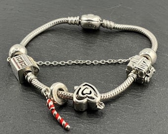 May include: A silver charm bracelet with a silver chain and several charms, including a house, a heart, and a candy cane.