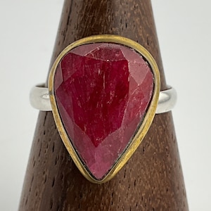 Peut inclure: Une bague avec une grande pierre précieuse de rubis rouge facetté sertie dans une bélière en or. La bague est en argent et a une bande simple.