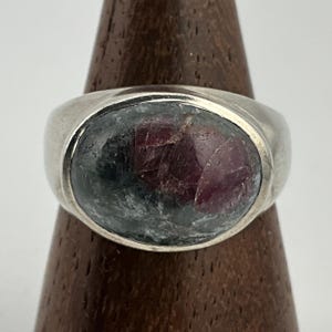 Può includere: Un anello d'argento con una grande pietra preziosa di forma ovale. La pietra preziosa è un mix di verde scuro e rosa.
