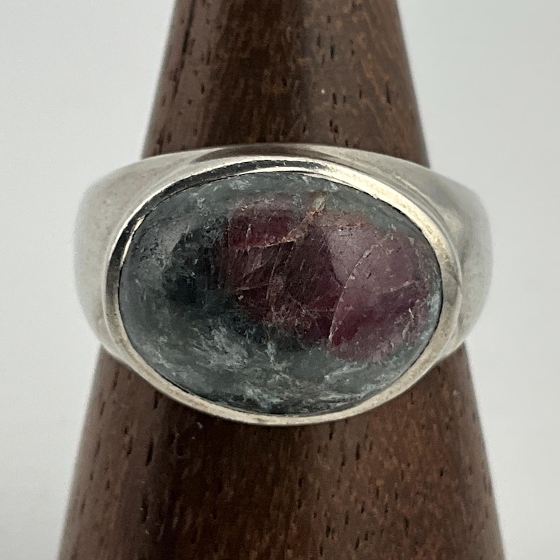 May include: A silver ring with a large oval-shaped gemstone. The gemstone is a mix of dark green and pink.