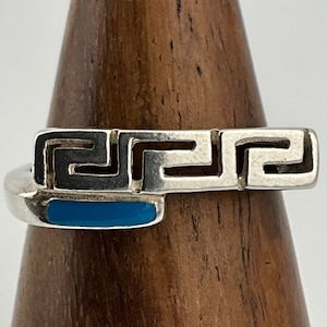 May include: A silver ring featuring a blue turquoise inlay and a Greek key design.
