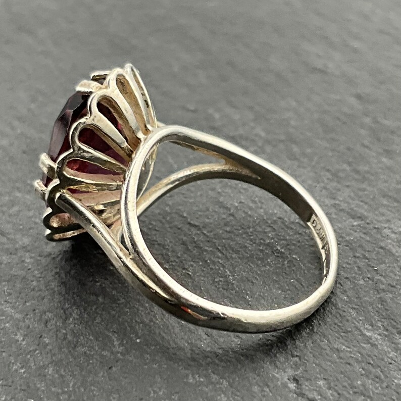 May include: A silver ring with a large, dark purple gemstone set in a crown-like design. The ring is made of sterling silver and has a polished finish.