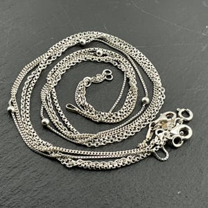 Puede incluir: Un conjunto de seis collares de cadena de plata con diferentes longitudes y estilos. Cada collar tiene una pequeña cuenta de plata en el extremo.