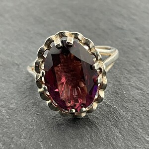 May include: A silver ring with a large, oval-shaped, purple gemstone set in a decorative, scalloped bezel.