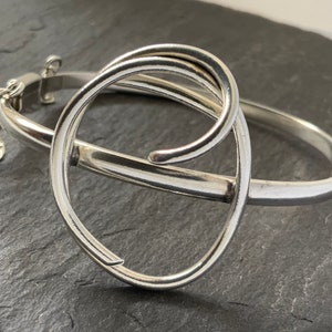 May include: A silver bangle bracelet with a unique, twisted design. The bracelet is open and has a hinged clasp.