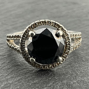 May include: A silver ring with a large black gemstone surrounded by a halo of smaller clear stones.