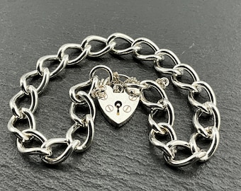 May include: A silver-toned bracelet with a heart-shaped padlock clasp. The bracelet features a chain link design. The padlock has a keyhole and decorative details. The bracelet is displayed on a dark surface.