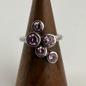 Può includere: Un anello d'argento con sei pietre preziose rosa incastonate in un design a grappolo.