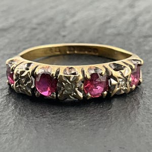 Può includere: Un anello in oro con una fila di rubini rossi rotondi e piccoli diamanti chiari alternati, incastonati in montature di metallo a forma di stella. L'interno dell'anello in oro presenta marchi e punzoni visibili.