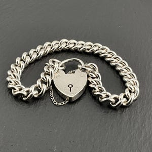 Puede incluir: Un brazalete de plata con un candado en forma de corazón y un diseño de cadena curb. El brazalete está hecho de plata de ley y tiene un aspecto clásico.