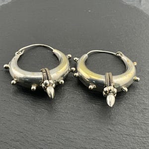 May include: A pair of silver hoop earrings with a pointed detail at the bottom. The hoops are decorated with small silver beads.