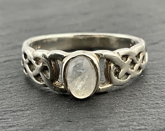 May include: A silver ring with a Celtic knot design and a clear moonstone oval gemstone.