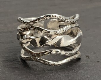 May include: A silver ring with a wavy, textured design. The ring is made of multiple bands that are intertwined and have a hammered finish.