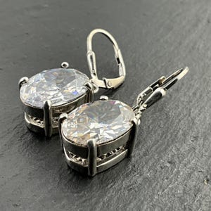 May include: A pair of silver dangle earrings with large oval-shaped clear cubic zirconia stones.