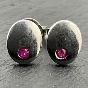 May include: A pair of silver earrings with a small pink gemstone set in each earring.