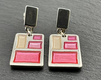 May include: A pair of silver dangle earrings with a geometric design. The earrings feature a rectangular shape with multiple squares inside, filled with pink and beige enamel.