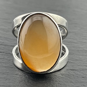 May include: A silver ring featuring a large oval-shaped, light brown gemstone set in the centre. The ring has a double band design.