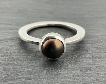 May include: A silver ring with a dark brown pearl set in a bezel setting.