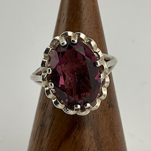 May include: A silver ring with a large, oval-shaped, purple gemstone set in a decorative, scalloped bezel.