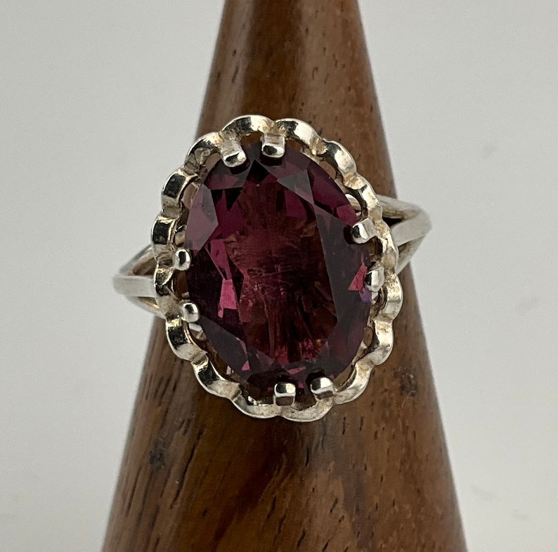 May include: A silver ring with a large, oval-shaped, purple gemstone set in a decorative, scalloped bezel.