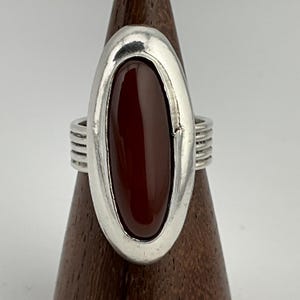 May include: A silver ring with a large oval carnelian stone set in a bezel setting. The ring has a textured band.