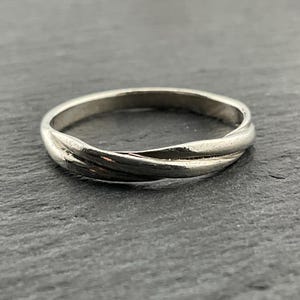 May include: A silver band ring with a twisted design. The ring is smooth and polished.