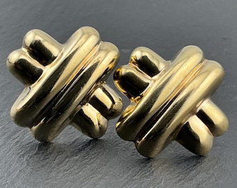 Pode incluir: Um par de brincos em tom dourado polido com um design de cruz simétrica de quatro pontas com segmentos tubulares arredondados. Os brincos têm um acabamento metálico liso e reflexivo com uma estrutura dimensional e em camadas em forma de X.
