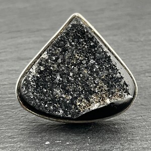 May include: A silver ring featuring a black, sparkly, triangular stone.