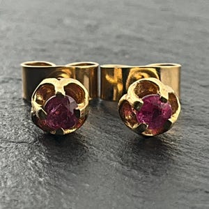 Peut inclure: Une paire de boucles d'oreilles à clous en or avec des pierres précieuses rondes, facettées et rose foncé, montées sur un sertissage à quatre griffes. Les boucles d'oreilles ont une finition dorée polie et un fermoir à tige classique.