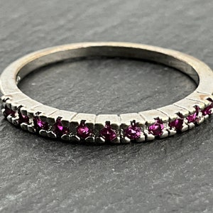 Könnte beinhalten: Ein silberner Bandring mit einer Reihe kleiner rosa Edelsteine.