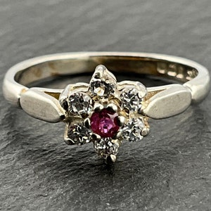 May include: A silver ring featuring a pink gemstone surrounded by smaller clear gemstones in a flower design.