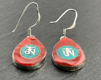 May include: A pair of silver dangle earrings with red coral and turquoise accents. The earrings feature a silver Om symbol in the center of each coral drop.