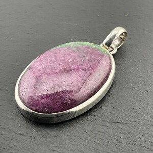 May include: A silver pendant featuring a large oval green and purple gemstone.