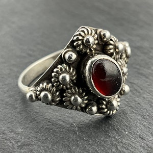 May include: A silver ring featuring a red gemstone set within a floral design.