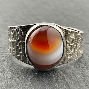 May include: A silver ring with a textured band and a large, round, brown and white agate stone.