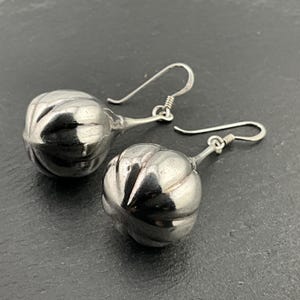 May include: A pair of silver earrings with a round, textured, bulbous design. The earrings have a simple hook closure.