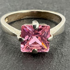 May include: A silver ring with a square pink gemstone.