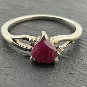 Puede incluir: Un anillo de plata con una piedra preciosa de rubí en forma de corazón y dos pequeños acentos de diamantes.