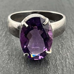 May include: A silver ring with a large, oval-shaped amethyst gemstone. The ring has a textured band.
