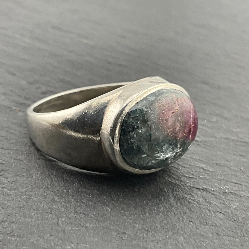 May include: A silver ring with a large oval-shaped green, pink, and clear gemstone.
