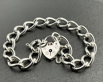 May include: A silver-toned bracelet with a heart-shaped padlock clasp. The bracelet features a chain link design with a secure clasp. The padlock has a keyhole and decorative details. The bracelet is displayed on a dark surface.