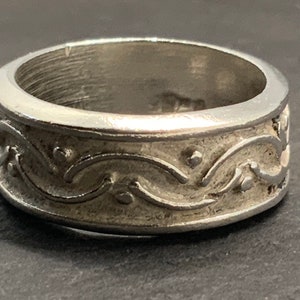 May include: A silver ring with a decorative, swirling design. The ring is wide and has a smooth, polished finish.