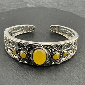 May include: A silver bangle bracelet with an intricate floral design and yellow gemstone accents.