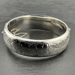 Peut inclure: Un bracelet jonc en argent avec un motif floral. Le bracelet est gravé avec "925 Sterling Silver".