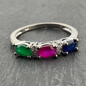 May include: A silver ring featuring three oval-shaped gemstones. The gemstones are green, pink, and blue.